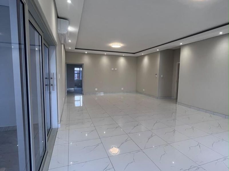 Spacious, modern open-plan living area featuring polished marble-look porcelain tiles, recessed ceiling lighting, and large sliding glass doors providing ample natural light.
