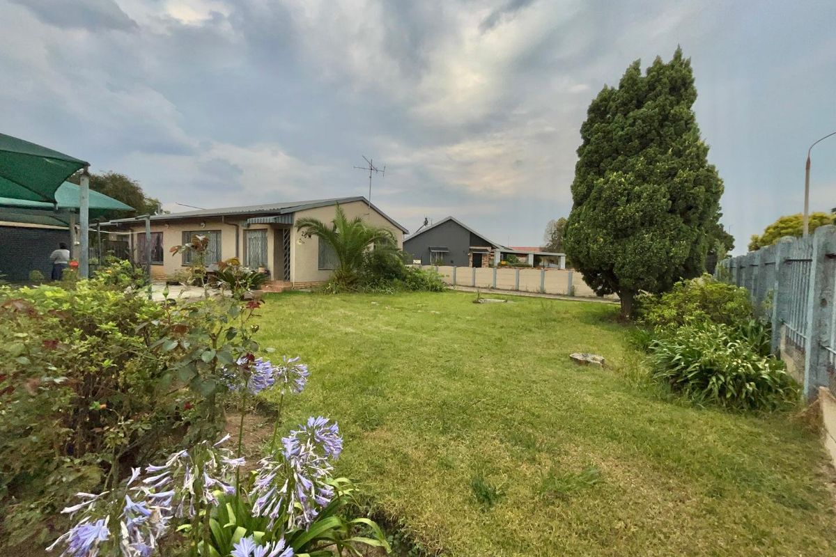 A spacious rear garden featuring a well-maintained lawn, established landscaping, and a view of the rear building elevation with a covered patio area.