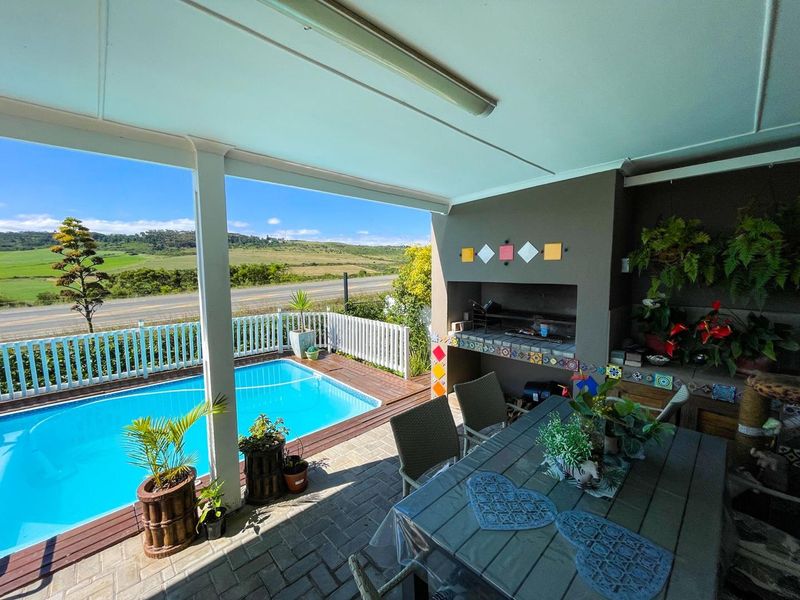 Covered outdoor patio featuring a built-in braai, paved flooring, and direct access to a swimming pool with scenic landscape views.