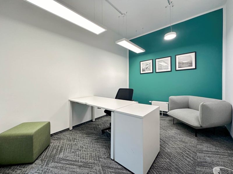 A modern office space featuring a vibrant teal accent wall, professional linear and pendant lighting, and durable carpet flooring.