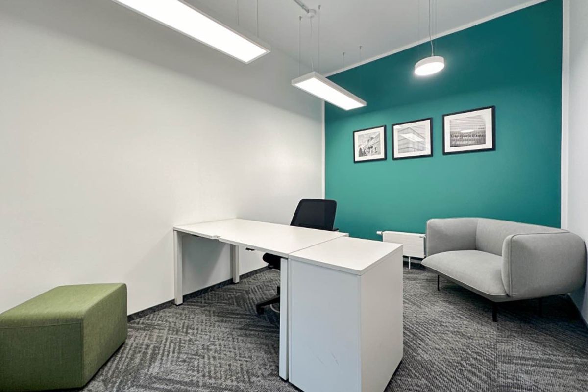 A modern office space featuring a vibrant teal accent wall, professional linear and pendant lighting, and durable carpet flooring.