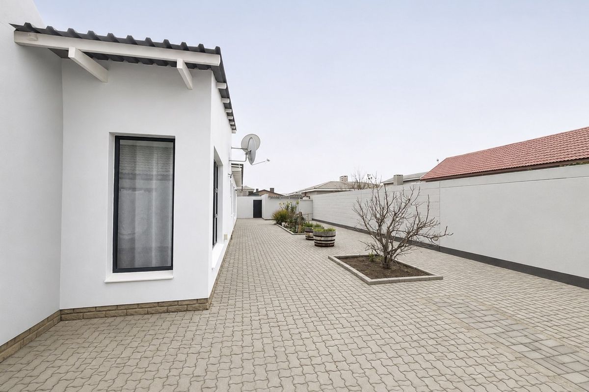 A clean, paved rear courtyard area featuring a boundary wall, established garden bed, and modern exterior finishes.
