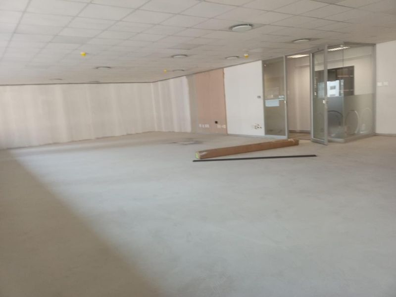 An open-plan office space featuring a suspended ceiling, recessed lighting, and a glass-partitioned meeting room, currently in a shell condition.