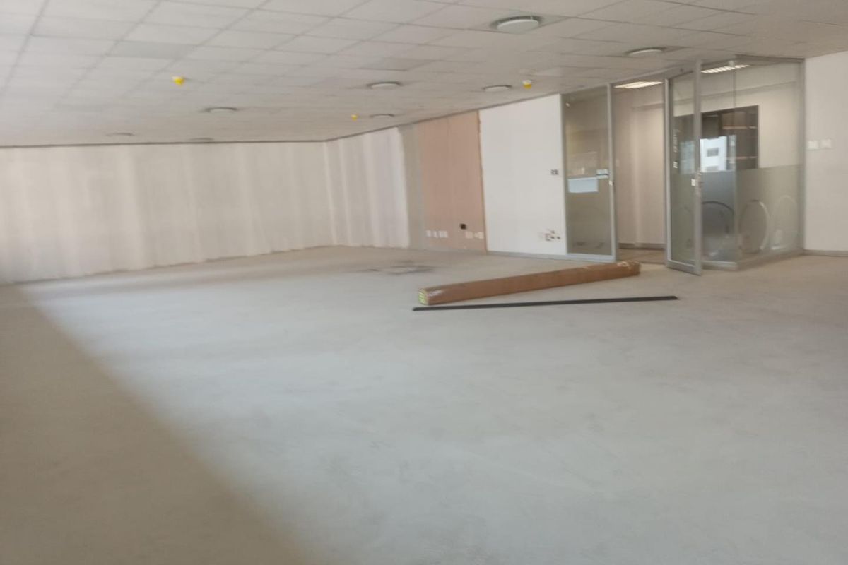 An open-plan office space featuring a suspended ceiling, recessed lighting, and a glass-partitioned meeting room, currently in a shell condition.