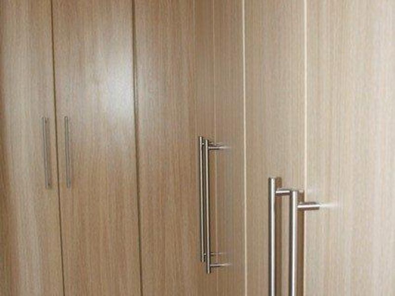 A clean bedroom interior featuring modern light wood-finish built-in cupboards and neutral tiled flooring.