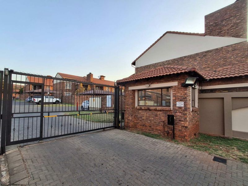 Entrance view of the apartment complex featuring a secure gated access point, brick guard house, and paved driveway.