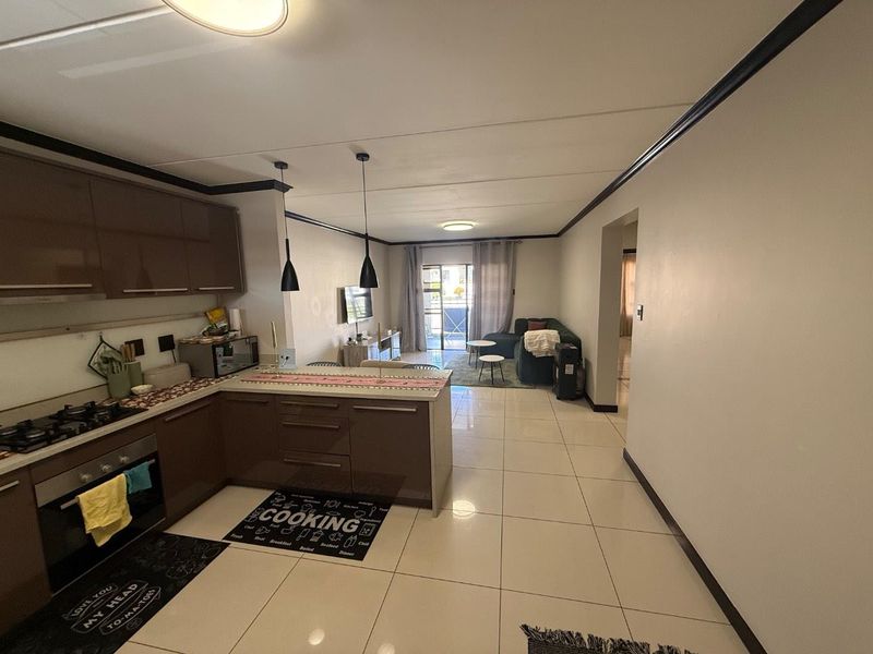Open-plan living area featuring a modern kitchen with built-in cabinetry, gas hob, and oven, flowing into a bright lounge with access to a balcony.