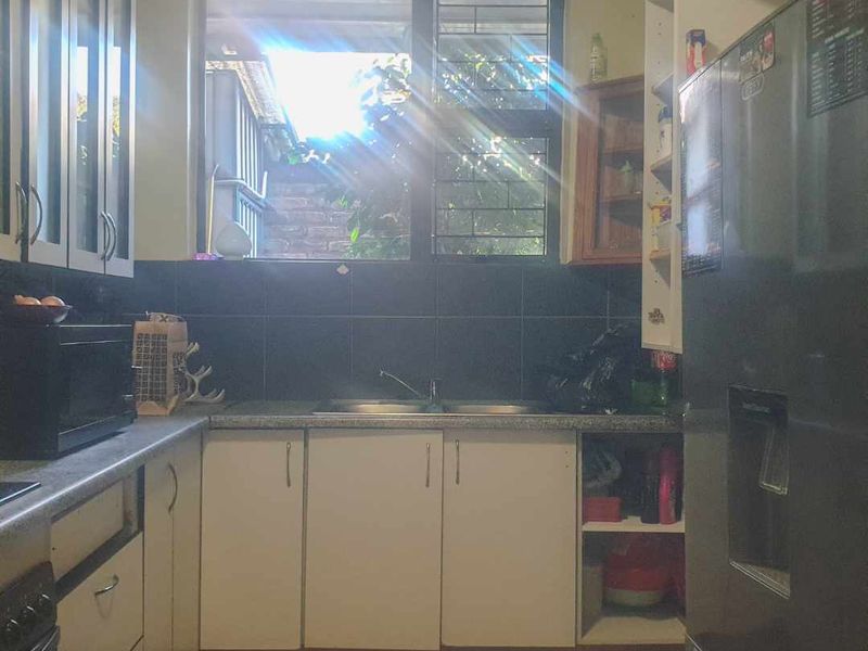A functional kitchen featuring white cabinetry, dark tiled backsplash, double sink, and tiled flooring with natural light from the window.