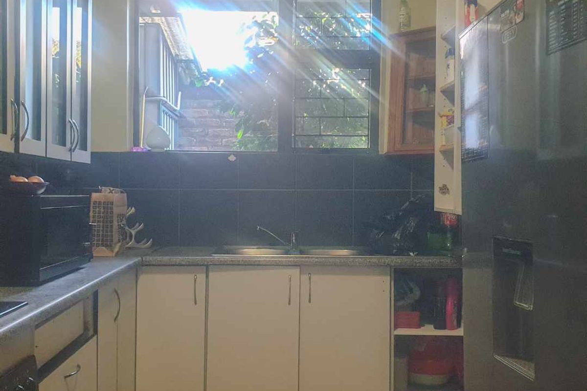 A functional kitchen featuring white cabinetry, dark tiled backsplash, double sink, and tiled flooring with natural light from the window.