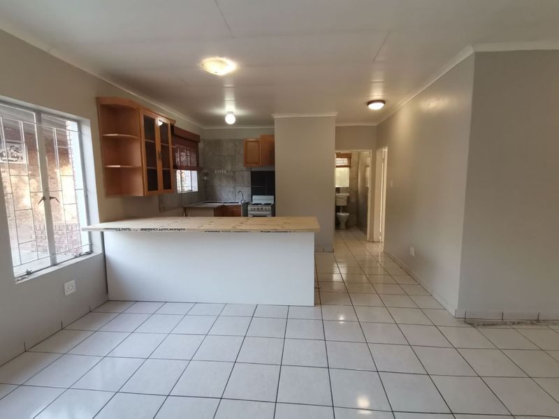 Open plan kitchen and living area featuring tiled flooring, built-in cabinetry, and a breakfast bar, leading to a hallway and bathroom.