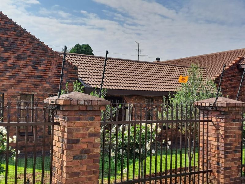 Front view of a well-maintained face brick house featuring a tiled roof, secure perimeter wall with metal fencing, and integrated electric security system.