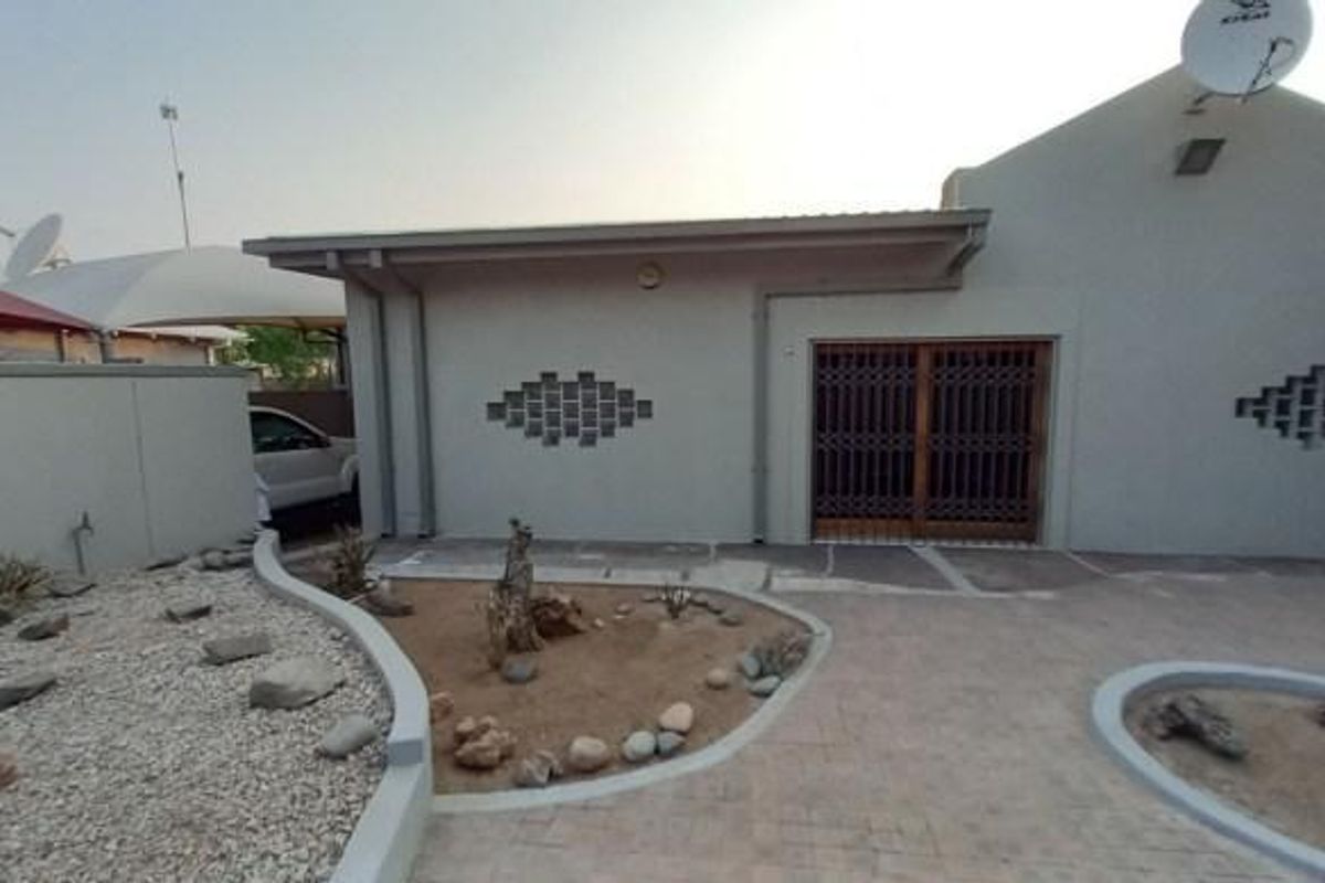 Rear exterior view of the property featuring a paved patio area, low-maintenance landscaped garden beds, and a secure sliding door entrance.