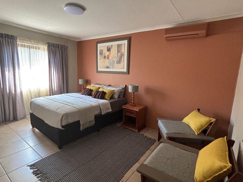 A spacious bedroom featuring tiled flooring, a wall-mounted air conditioning unit, and neutral wall tones, offering a comfortable and functional living space.