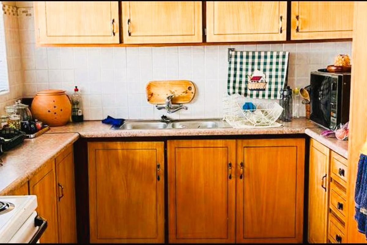 A compact kitchen featuring wooden cabinetry, a double-basin sink, and tiled splashbacks, offering a functional layout with potential for modern updates.