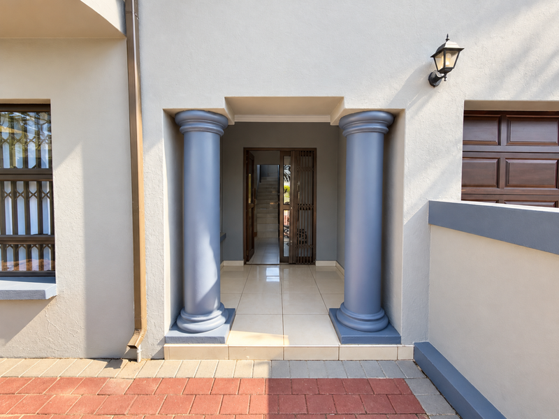 A well-maintained front entrance featuring decorative columns, tiled porch flooring, and a secure entrance gate with exterior lighting.