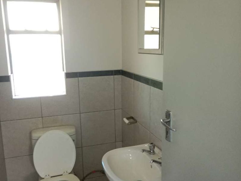 A functional bathroom featuring a pedestal basin, toilet, and tiled wall finishes with a neutral aesthetic.