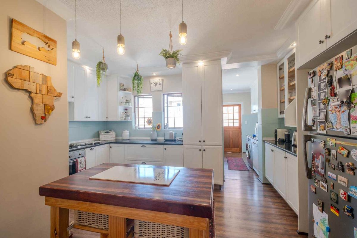A bright kitchen featuring white cabinetry, dark countertops, a central wooden island, and a connected laundry area with direct exterior access.