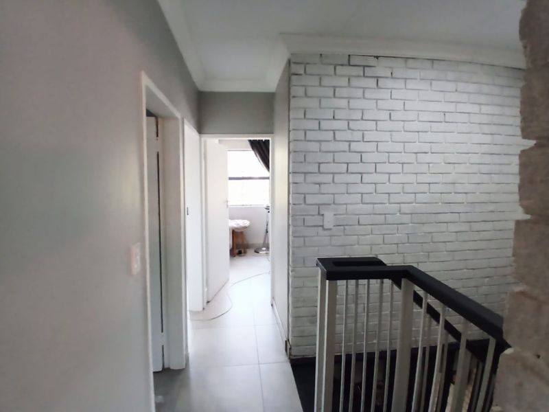 A bright hallway featuring a white-painted brick accent wall, tiled flooring, and a modern staircase balustrade leading to adjacent rooms.