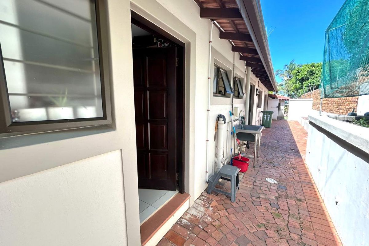 A side exterior walkway featuring brick paving, a utility sink, and access to the main dwelling through a dark wood door.