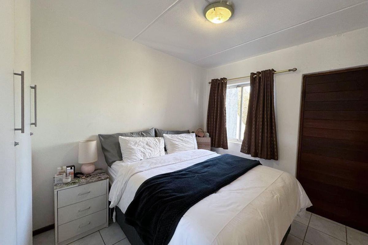 A functional bedroom featuring tiled flooring, built-in wardrobe storage, and a window with curtain rod.