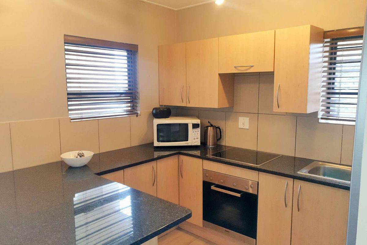 Compact kitchen featuring light wood cabinetry, dark granite countertops, built-in oven, electric hob, and tiled backsplash with natural light from dual windows.