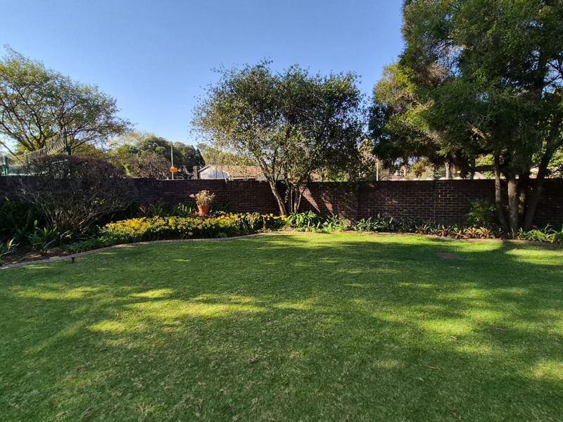 A well-maintained private garden featuring a lush green lawn, established trees, and a solid brick boundary wall.