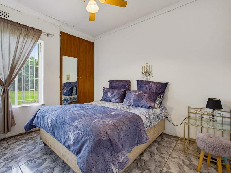 A bedroom featuring tiled flooring, a built-in wardrobe, and a ceiling fan, with security bars installed on the window.
