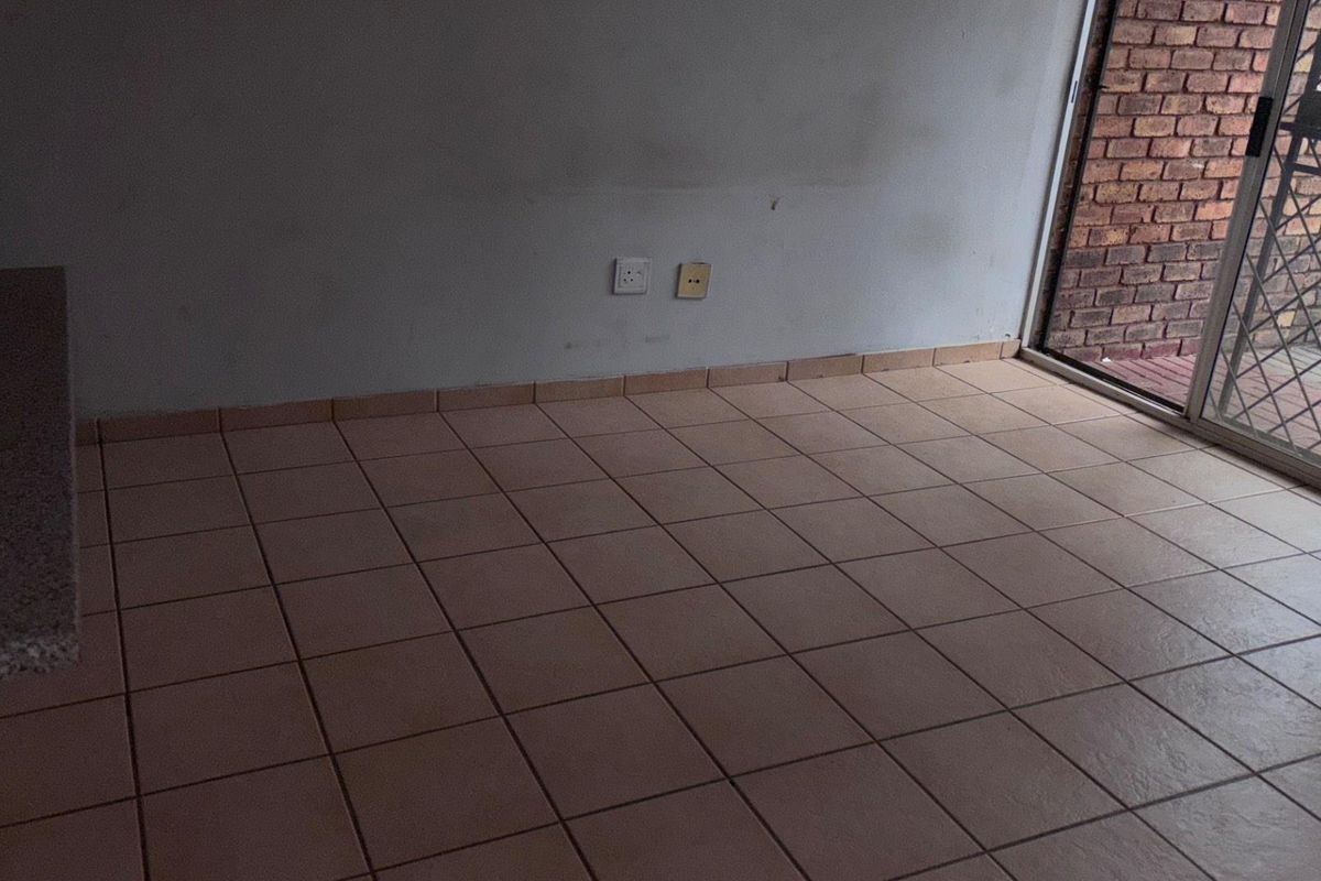 An empty living area featuring ceramic floor tiles and a sliding glass door with a security gate leading to an outdoor space.