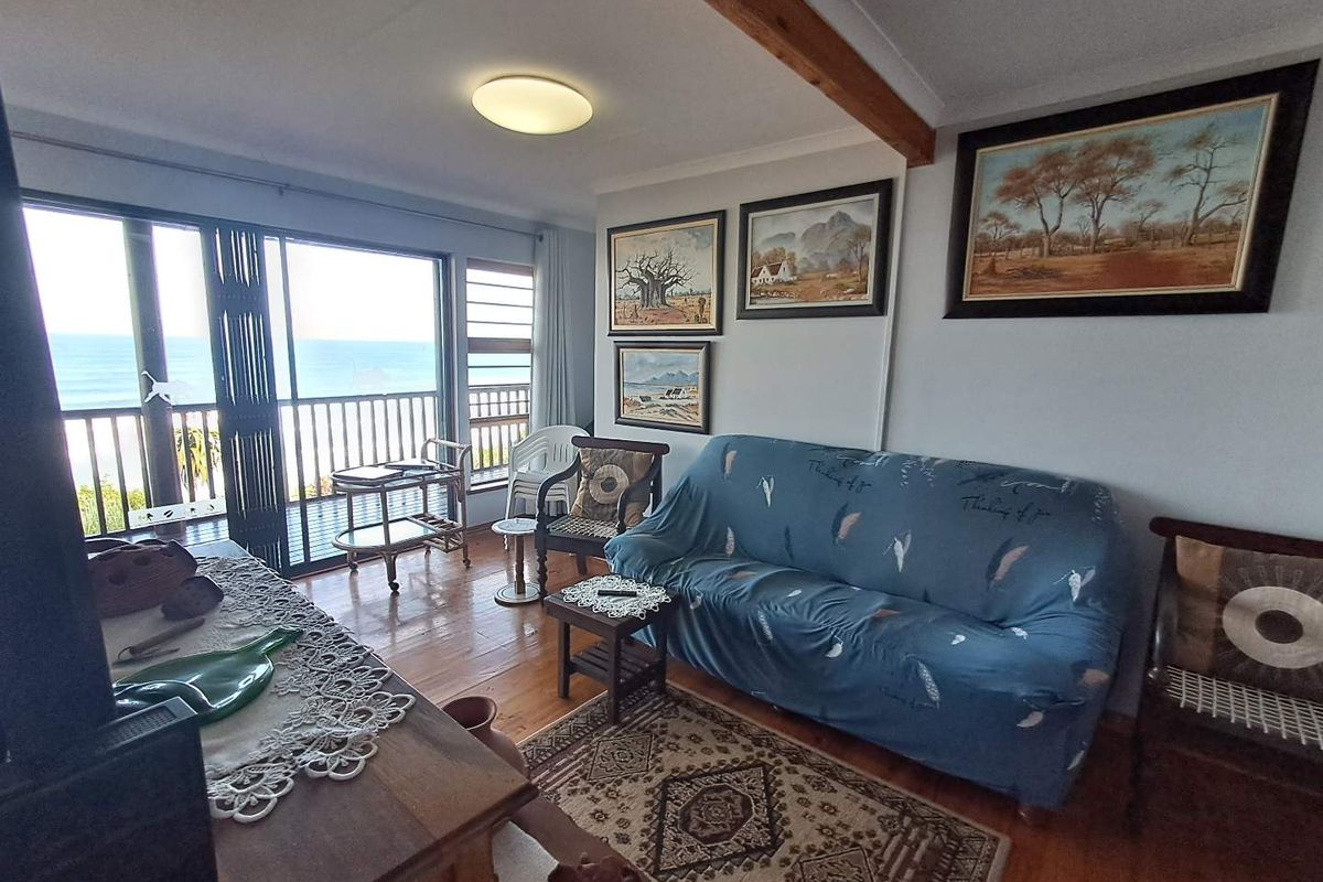 A living room featuring timber flooring, an exposed ceiling beam, and large sliding glass doors opening onto a balcony with ocean views.