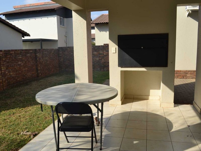 A covered patio area featuring a built-in braai, tiled flooring, and direct access to the rear garden with brick boundary walls.