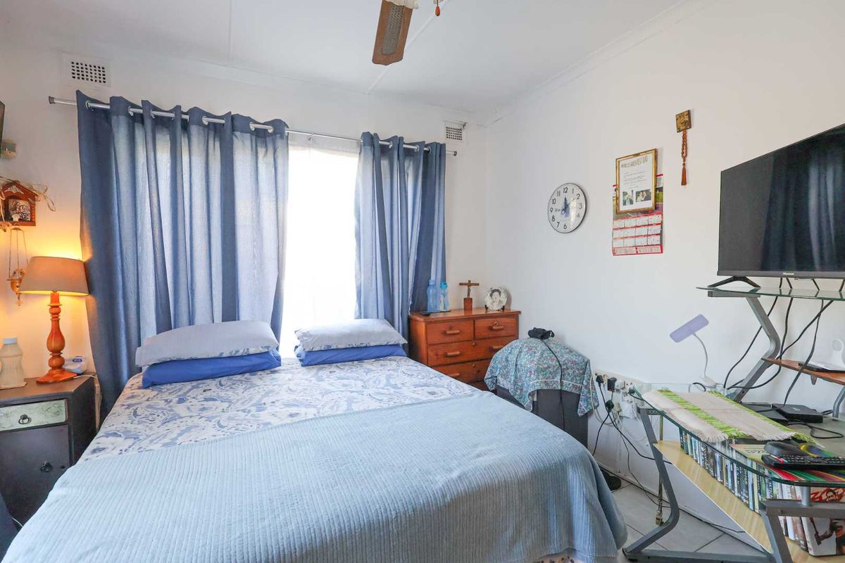 A functional bedroom featuring a window with curtain tracks, ceiling fan, and tiled flooring.