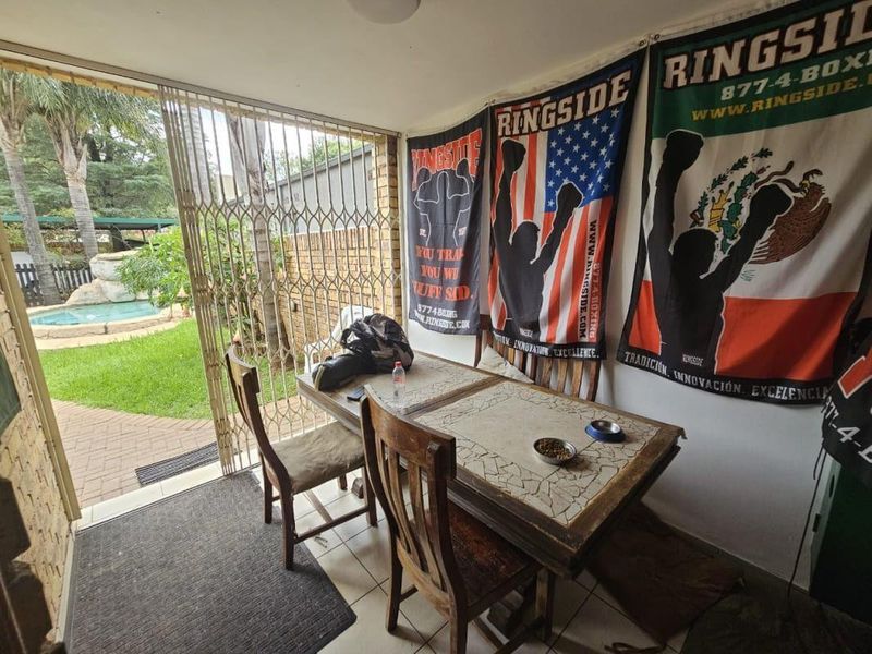 A covered patio area featuring tiled flooring and a security gate, providing direct access to the garden and pool area.