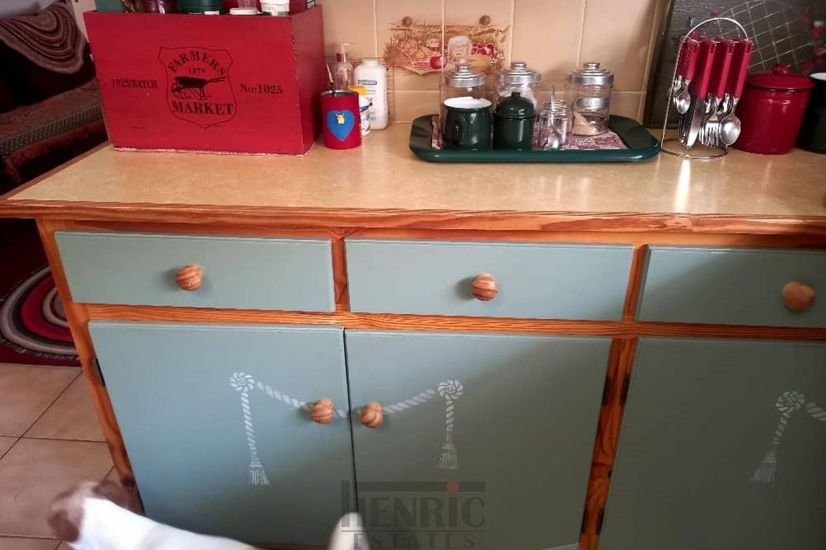 A kitchen base cabinet unit featuring painted wooden doors, wooden knobs, and a laminate countertop with tiled splashback.