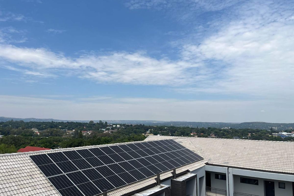 Aerial view of an apartment building roof featuring a large installed solar panel array and surrounding suburban landscape.