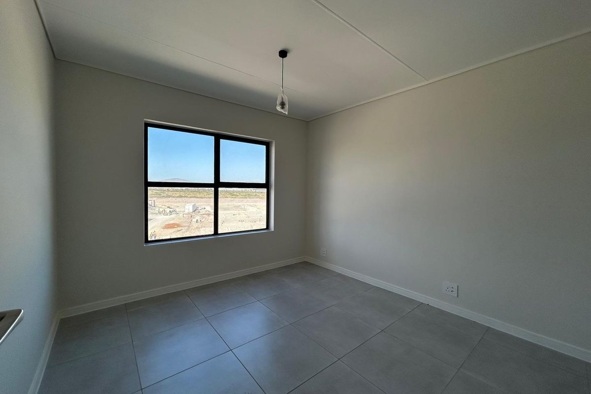 A bright, empty bedroom featuring neutral tiled flooring, clean white walls, and a large window offering an expansive exterior view.