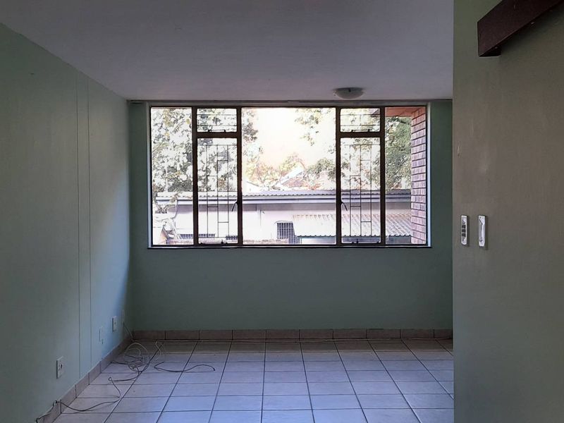 An empty living room featuring tiled flooring and a large window with security bars, offering a blank canvas for potential interior design updates.