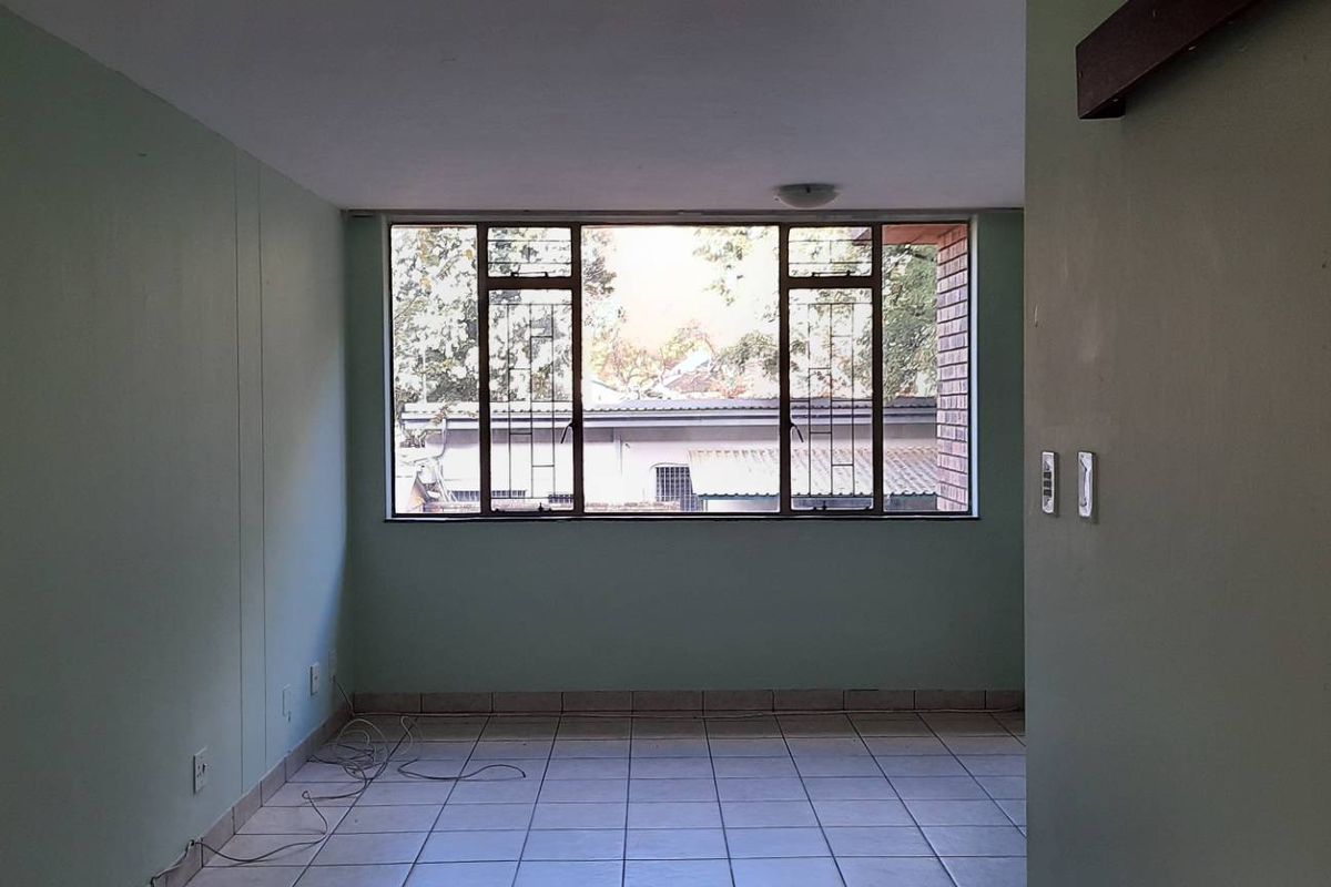 An empty living room featuring tiled flooring and a large window with security bars, offering a blank canvas for potential interior design updates.