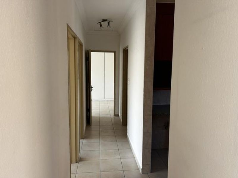 A clean, tiled hallway providing access to multiple rooms, featuring neutral walls and built-in storage cupboards.