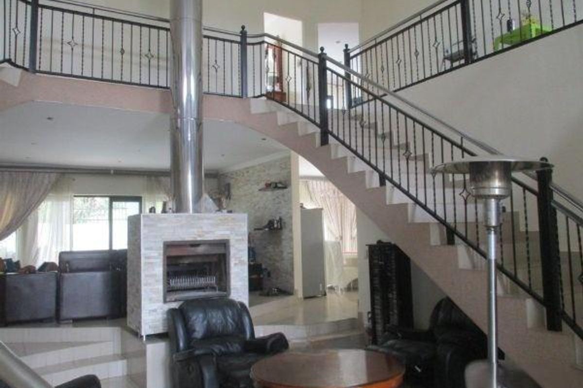 Spacious living area featuring a prominent central fireplace with stainless steel flue and an elegant staircase with wrought iron railings.