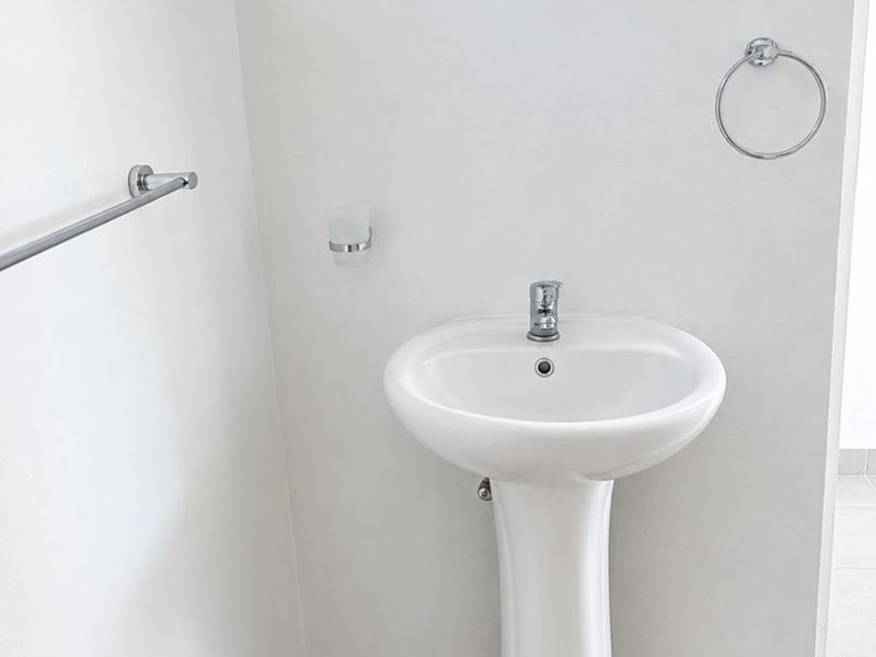 A clean and modern bathroom featuring a white pedestal basin with chrome fixtures and neutral floor tiling.
