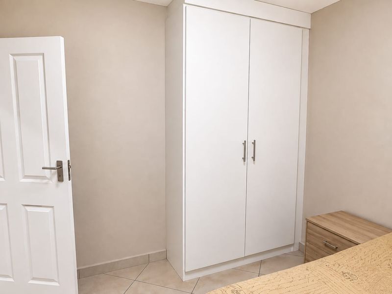 A clean bedroom featuring neutral walls, tiled flooring, and a white built-in wardrobe with modern hardware.