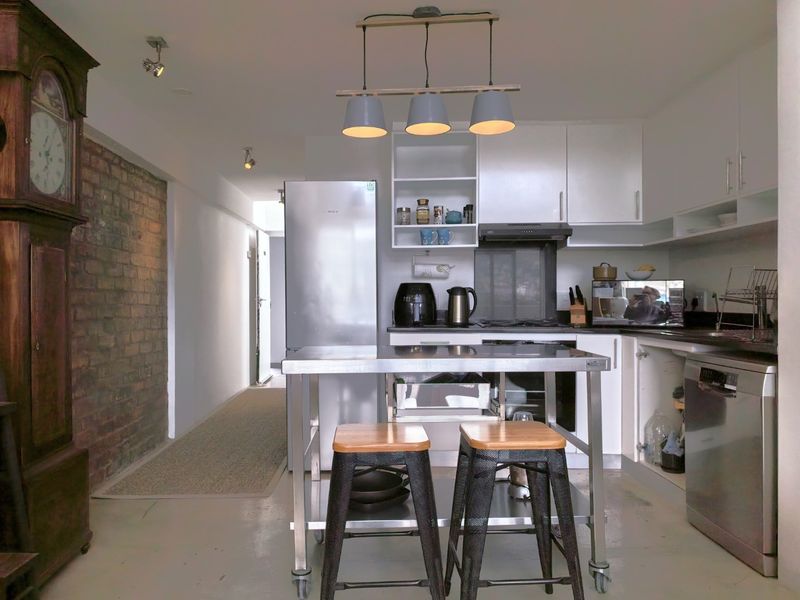 Modern kitchen featuring white cabinetry, stainless steel appliances, and a striking exposed brick wall, creating a contemporary industrial aesthetic.
