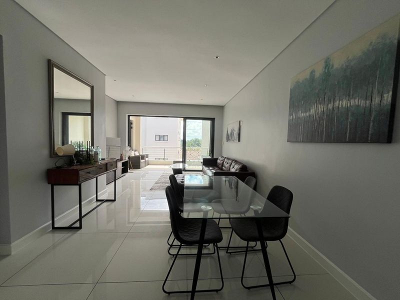 Spacious open-plan living and dining area featuring large format porcelain tiles, recessed lighting, and seamless access to a private balcony through sliding glass doors.