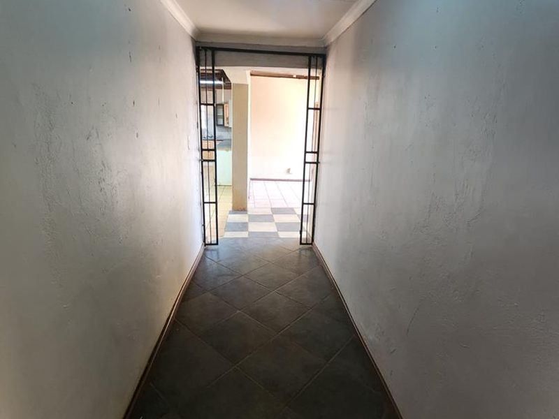 A narrow hallway featuring dark tiled flooring and a metal security gate leading into an adjacent living space.