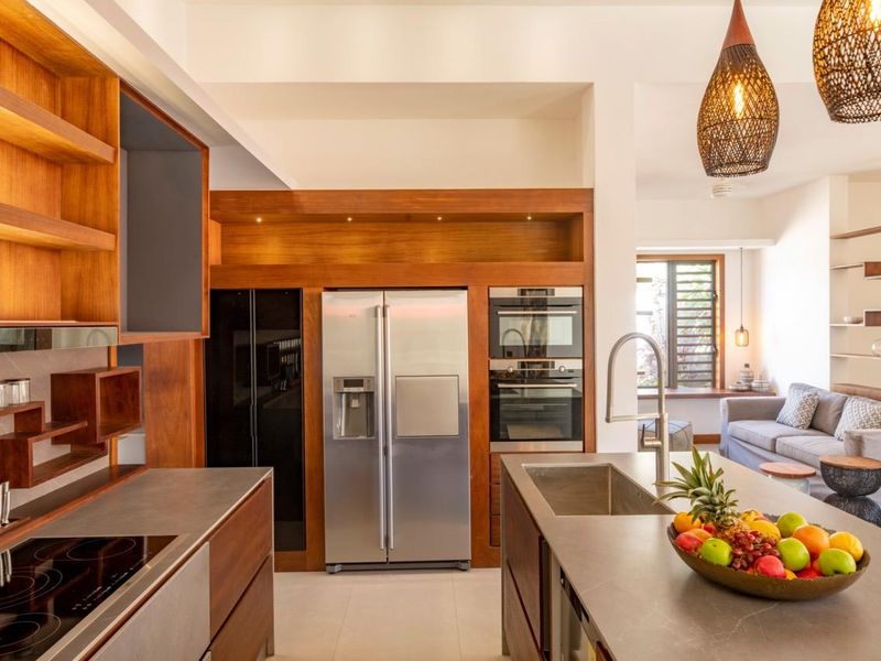Modern open-plan kitchen featuring high-end cabinetry, integrated appliances, stone countertops, and a central island with a sink, flowing into the adjacent living area.