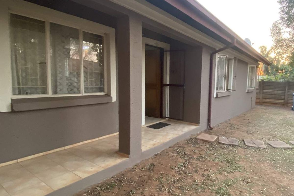 A rear exterior view of the townhouse featuring a covered tiled patio, security gate, and window burglar bars, overlooking a garden area.