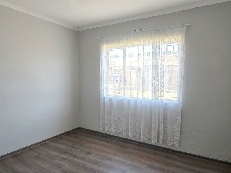 A bright, empty bedroom featuring laminate flooring, neutral walls, and a window fitted with security bars.