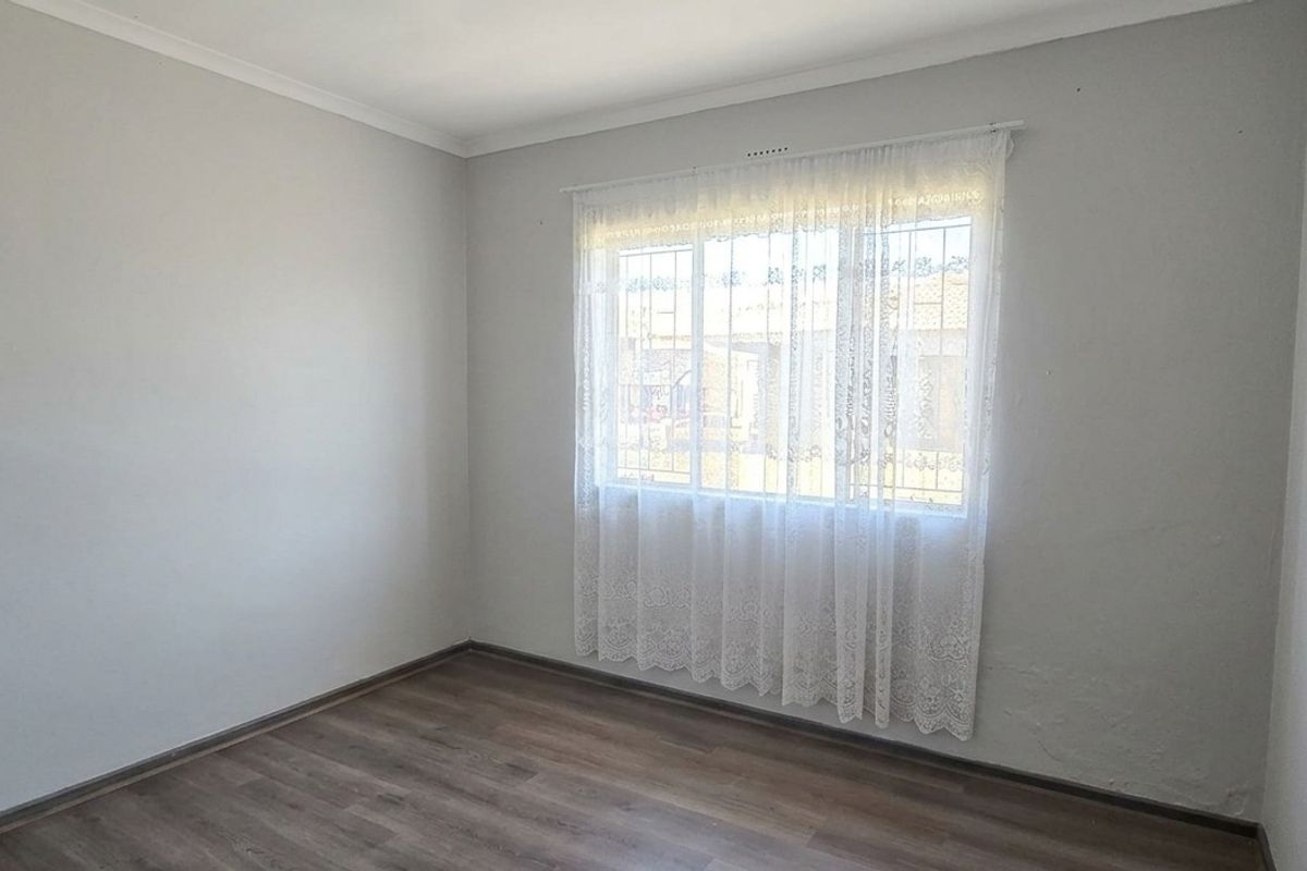 A bright, empty bedroom featuring laminate flooring, neutral walls, and a window fitted with security bars.