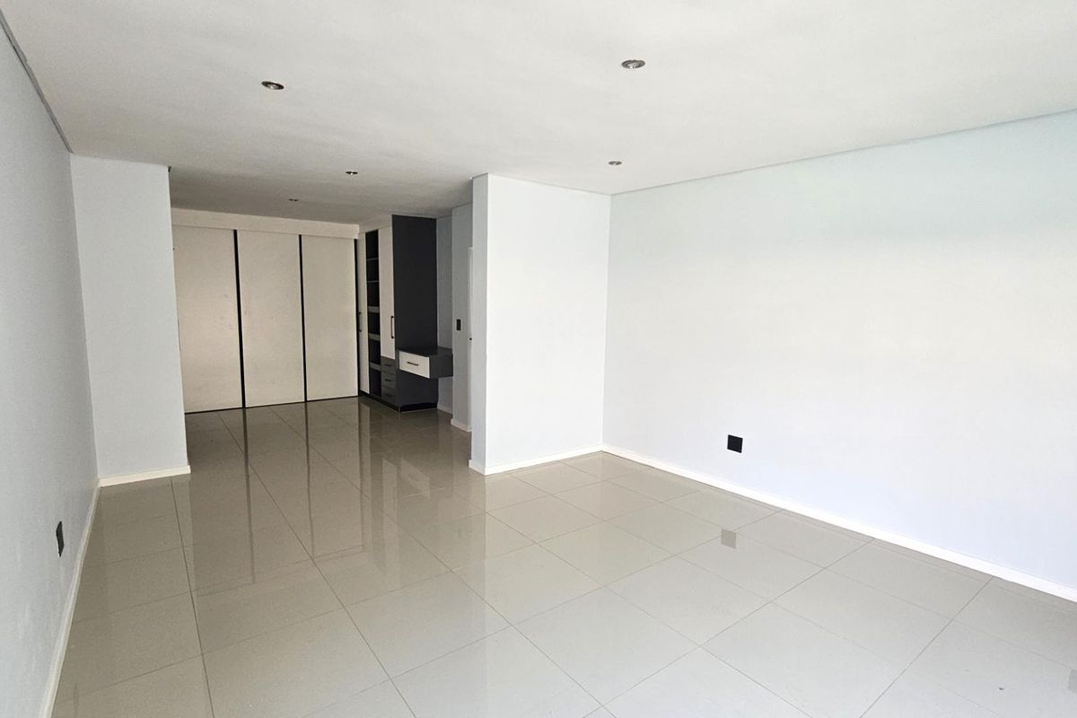 A spacious, empty bedroom featuring neutral tiled flooring, recessed ceiling lighting, and built-in cabinetry with integrated storage solutions.