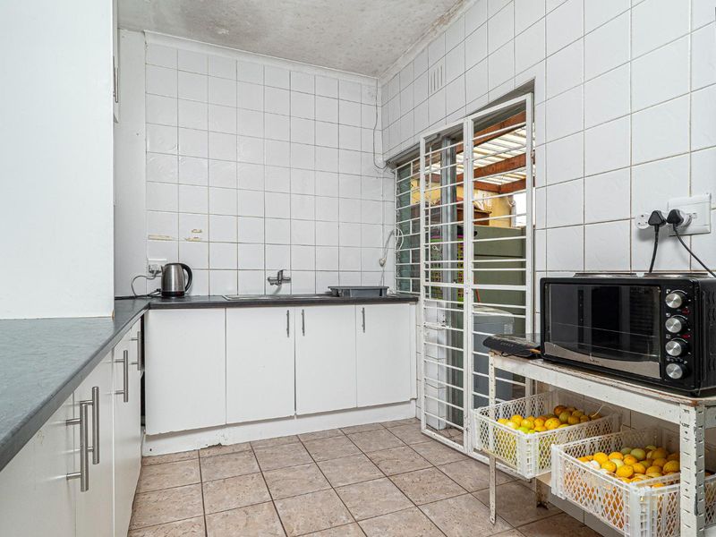 A functional scullery area featuring tiled walls, laminate countertops, built-in cabinetry, and a stainless steel sink, with direct access to an outdoor space.